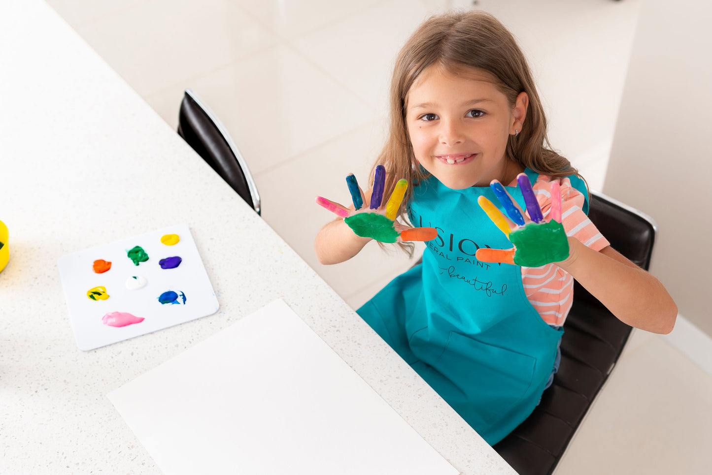 child with her hands full of paint Child Sized Paint Apronwhile wearing a paint apron